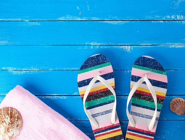 Paio di pantofole da spiaggia femminili e un asciugamano rosa su un retro blu — Foto Stock