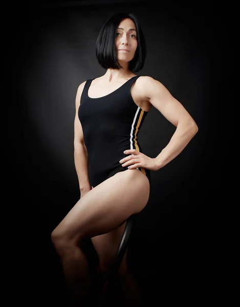 Jeune femme en body noir posant sur un fond sombre — Photo