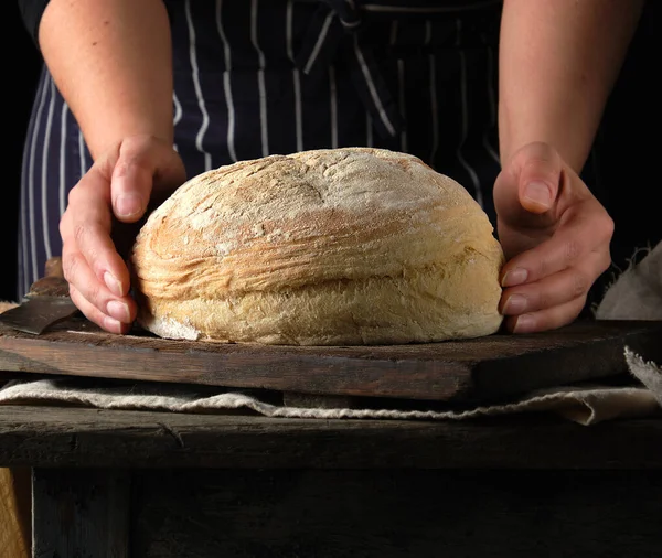 Mãos femininas segurando rodada pão de farinha de trigo assado sobre t de madeira — Fotografia de Stock