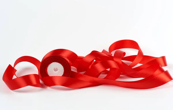 Zwinięte czerwone satynowe wstążki na białym tle, świąteczne tło — Zdjęcie stockowe