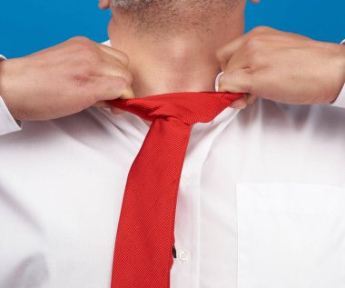 Beyaz ofis gömlekli bir adam mavi arka planda boynundan kırmızı saten bir kravat koparıyor. Depresyon, işsizlik ve işten çıkarma kavramı.