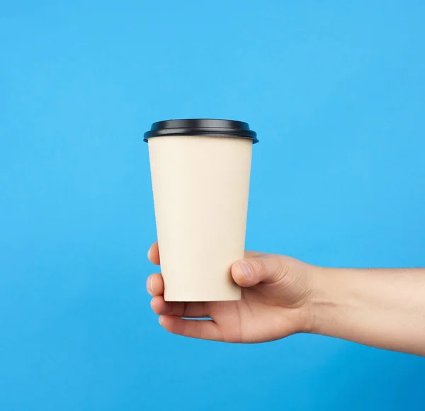 brown paper disposable cup with a plastic lid, female hand holds on a blue background
