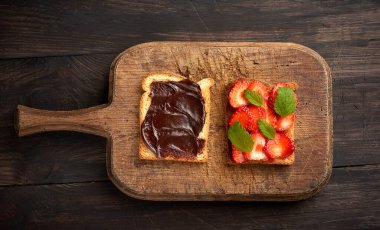 Kahverengi ahşap bir tahtanın üzerinde iki tost ve taze olgun kırmızı çilek, üst manzara, sabah kahvaltısı.