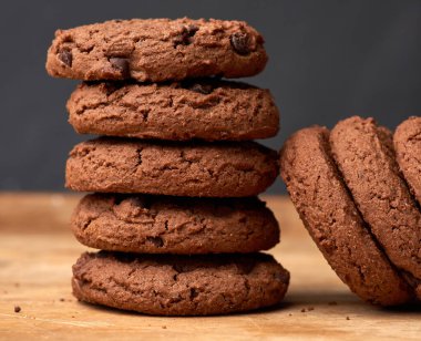 Kahverengi ahşap bir masada yuvarlak çikolatalı kurabiyeler yığını.