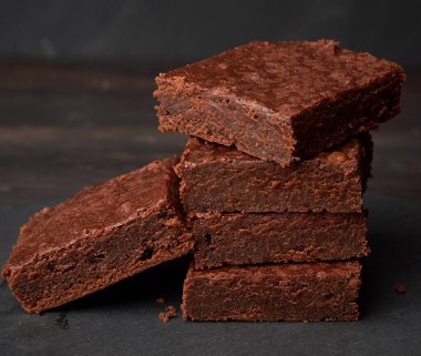 Bir yığın kare fırınlanmış çikolatalı kek siyah arka planda, lezzetli bir tatlı.