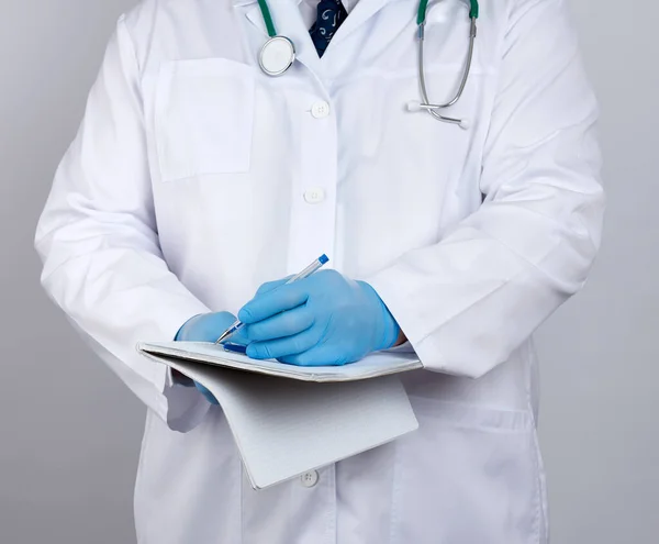 doctor in a white coat, blue latex sterile gloves holds an open yellow notebook in his hand on a white background, concept of recording the diagnosis when visiting patients