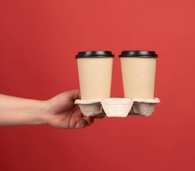 Tepside plastik kapaklı kahverengi kağıt bardaklar, kırmızı arka planda tek kullanımlık masa eşyaları.