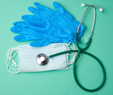 Yeşil arka planda mavi lateks eldivenler ve tek kullanımlık maskeler, salgın hastalıklar ve salgınlar için hijyen ve virüs koruma aksesuarları, genel görünüm