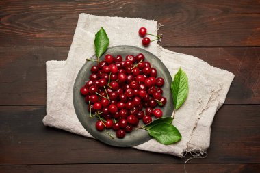 Kahverengi ahşap arka planda yuvarlak metal bir kasede olgun kırmızı kiraz.