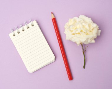 Beyaz çarşaflı, kırmızı ahşap kalemli ve mor arka planda beyaz güllü, düz bir defter.