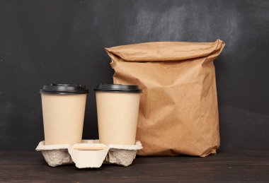 Kahverengi kağıt bardaklar, plastik kapaklı tepsi, ahşap masa, siyah arka plan, paket servis kapları.