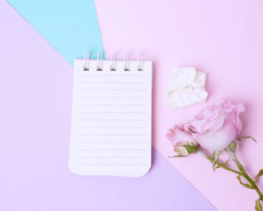 Üzerinde beyaz çarşaflar ve pembe bir gül bulunan açık bir defter.