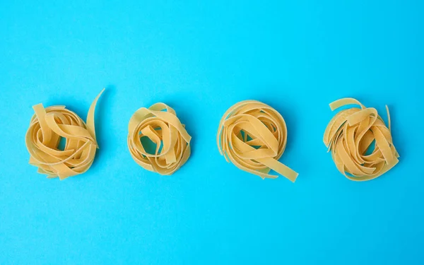 Skręcony Makaron Okrągłych Gniazdach Fettuccine Niebieskim Tle Kreatywne Tło Jedzeniem — Zdjęcie stockowe