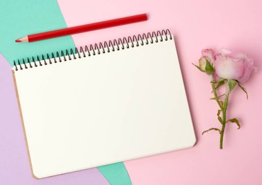 Üzerinde beyaz çarşaflar ve pembe bir gül bulunan açık bir defter.