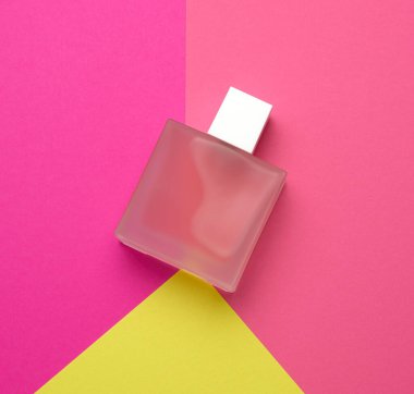 Buzlu cam parfümlü pembe şişe renkli bir arka planda yatar.