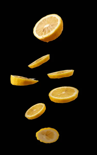 黒を背景に空中に浮遊する熟したジューシーな黄色のレモンのスライス 飲み物の成分 — ストック写真