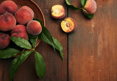 Yuvarlak kil bir tabakta olgun kırmızı şeftaliler ve kahverengi ahşap bir masada yeşil yapraklar, üst manzara, boşluk kopyala