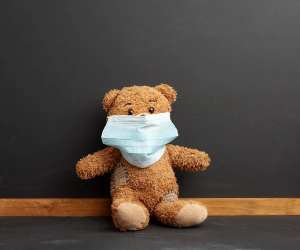 棕色的泰迪熊坐在黑色黑板背景的一次性医疗面罩上 在大流行病期间戴着面罩在学校上课 — 图库照片