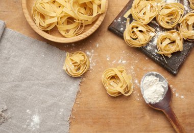 Kahverengi ahşap bir tahtada çiğ fettucine makarna ve ahşap bir eski model merdane.