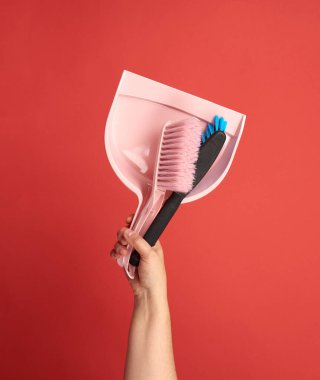 Kadın eli plastik kepçe tutuyor ve kırmızı arka planı fırçalıyor. Temizlik için eşyalar.