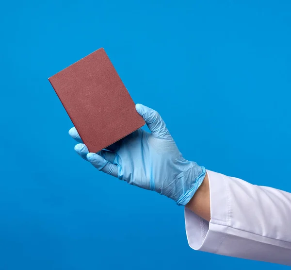 doctor in a blue latex glove holds a passport in a red cover on a blue background