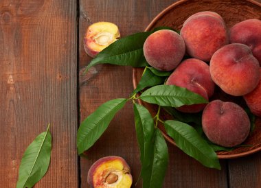 Yuvarlak bir tabakta olgun kırmızı şeftaliler ve kahverengi ahşap bir masada yeşil yapraklar.
