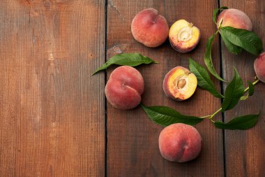 Olgun kırmızı şeftali ve yeşil yapraklar kahverengi ahşap bir masada, üst görünüm, boşluğu kopyala