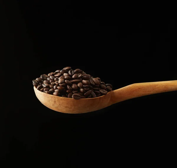 在黑色背景上的木制勺子中烘烤咖啡粒 — 图库照片