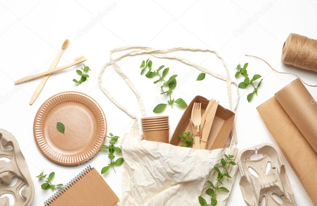 textile bag and disposable tableware from brown craft paper, green mint leaves on a whitebackground. View from above, plastic rejection concept, zero waste 