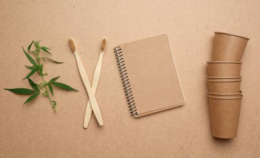 Tek kullanımlık kağıt bardaklar, not defteri ve ahşap çevresel diş fırçaları kahverengi arka plan, üst görüş, plastik reddetme konsepti, sıfır atık 