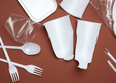 Plastik tabaklar, plastik parçalar ve kahverengi arka planda beyaz plastik bir torba, üst manzara, düz yatak. Plastik reddetme kavramı