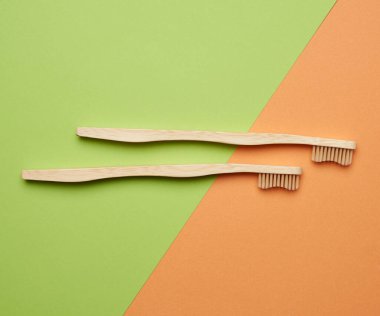 Yeşil turuncu arka planda iki tahta diş fırçası, plastik reddetme konsepti, sıfır atık 