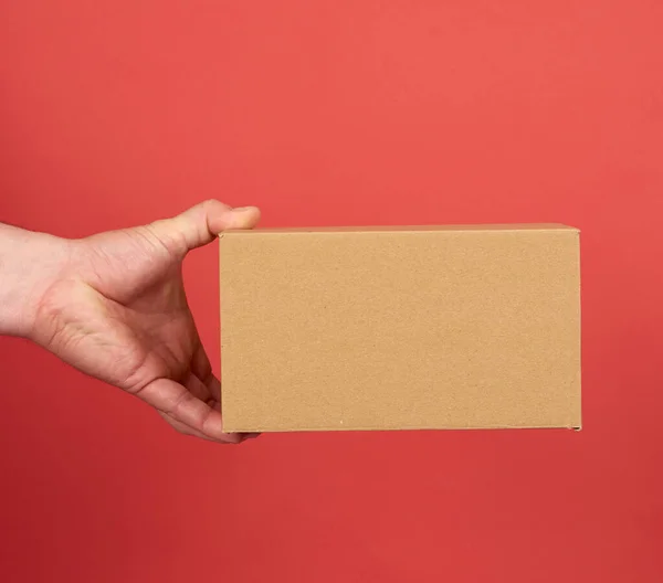 Mano Masculina Sostiene Una Caja Cartón Marrón Sobre Fondo Rojo —  Fotos de Stock