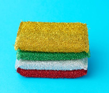 Mavi arka planda bulaşık yıkamak için çok renkli mutfak süngeri yığını.