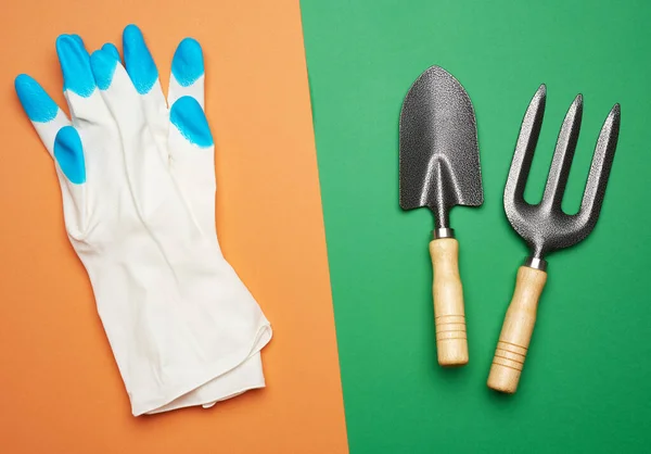 white rubber gloves and garden set of shovels, rakes, pitchforks on a green-orange background, top view, flat lay