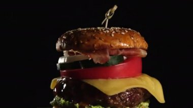 Domatesli çizburger, soğan, ızgara pirzola ve eski bir tahta kesim tahtasında susamlı ekmek, siyah arka plan. Fast food