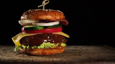 Domatesli çizburger, soğan, ızgara pirzola ve eski bir tahta kesim tahtasında susamlı ekmek, siyah arka plan. Fast food