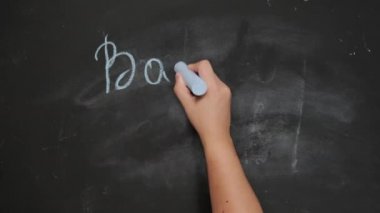 Kadın eli mavi tebeşiri tutuyor ve okula siyah tebeşirle geri yazıyor. Okul yılı başlıyor.