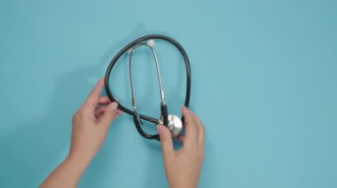 Kadın eli mavi arka planda tıbbi bir steteskop takıyor.