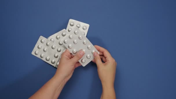 丸い錠剤をブリスターパックに入れ 2人の女性の手は青い背景に薬を入れ トップビュー — ストック動画