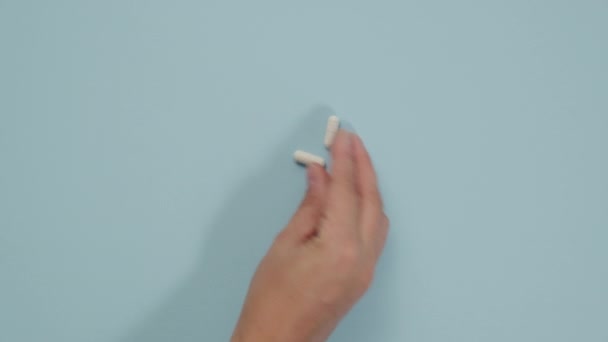 女性の手は青い背景に楕円形の白い丸薬を折る ブリスターパックの薬 トップビュー — ストック動画
