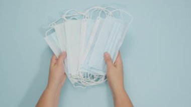 İki kadın eli mavi bir arkaplan takıyor tek kullanımlık tıbbi maske yığını, virüslere ve bakterilere karşı koruma, üst görünüm.