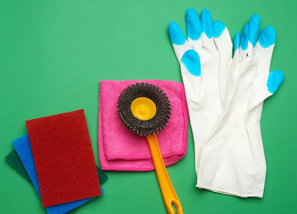white rubber gloves for cleaning, multi-colored sponges, brushes on a green background,  flat lay