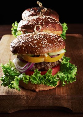Lezzetli hamburgerler, kızarmış sığır pirzolası, domates, marul ve soğan, susamlı beyaz buğday unlu çörek. Tahtadaki fast food.