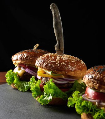Lezzetli hamburgerler, kızarmış sığır pirzolası, domates, marul ve soğan, susamlı beyaz buğday unlu çörek. Tahtadaki fast food.