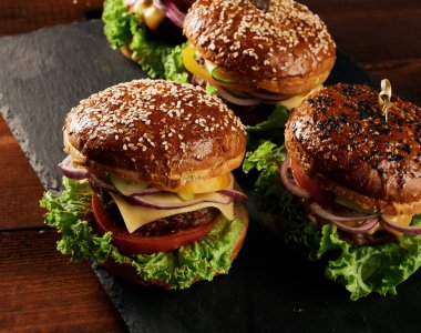 Lezzetli hamburgerler, kızarmış sığır pirzolası, domates, marul ve soğan, susamlı beyaz buğday unlu çörek. Tahtadaki fast food.