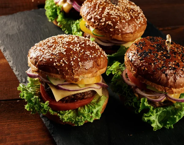 Lezzetli hamburgerler, kızarmış sığır pirzolası, domates, marul ve soğan, susamlı beyaz buğday unlu çörek. Tahtadaki fast food.
