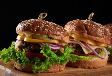 Lezzetli hamburgerler, kızarmış sığır pirzolası, domates, marul ve soğan, susamlı beyaz buğday unlu çörek. Tahtadaki fast food.