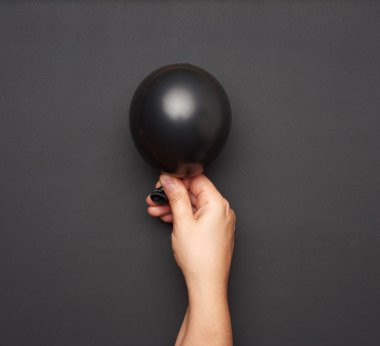 Siyah arka planda şişirilmiş siyah hava balonunu tutan kadın eli, yakın plan.