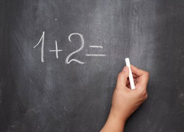Siyah tebeşirle beyaz tebeşirle yazılmış matematik örneği ve beyaz tebeşirli bir kadın eli, bir artı iki.
